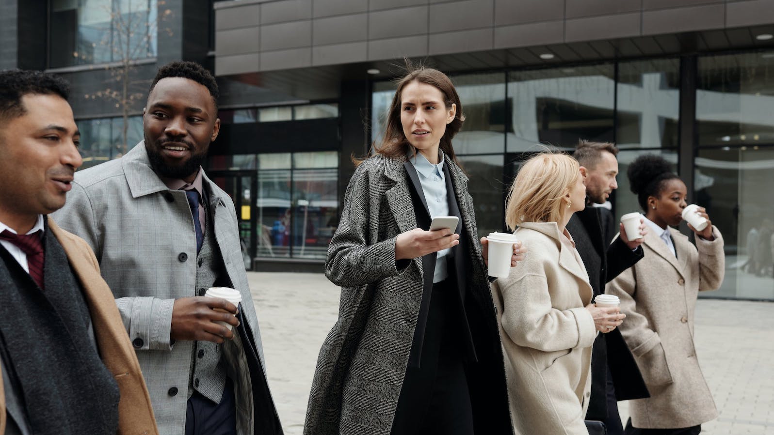 Six people in suits walking in a line and holding coffee as they go back to work