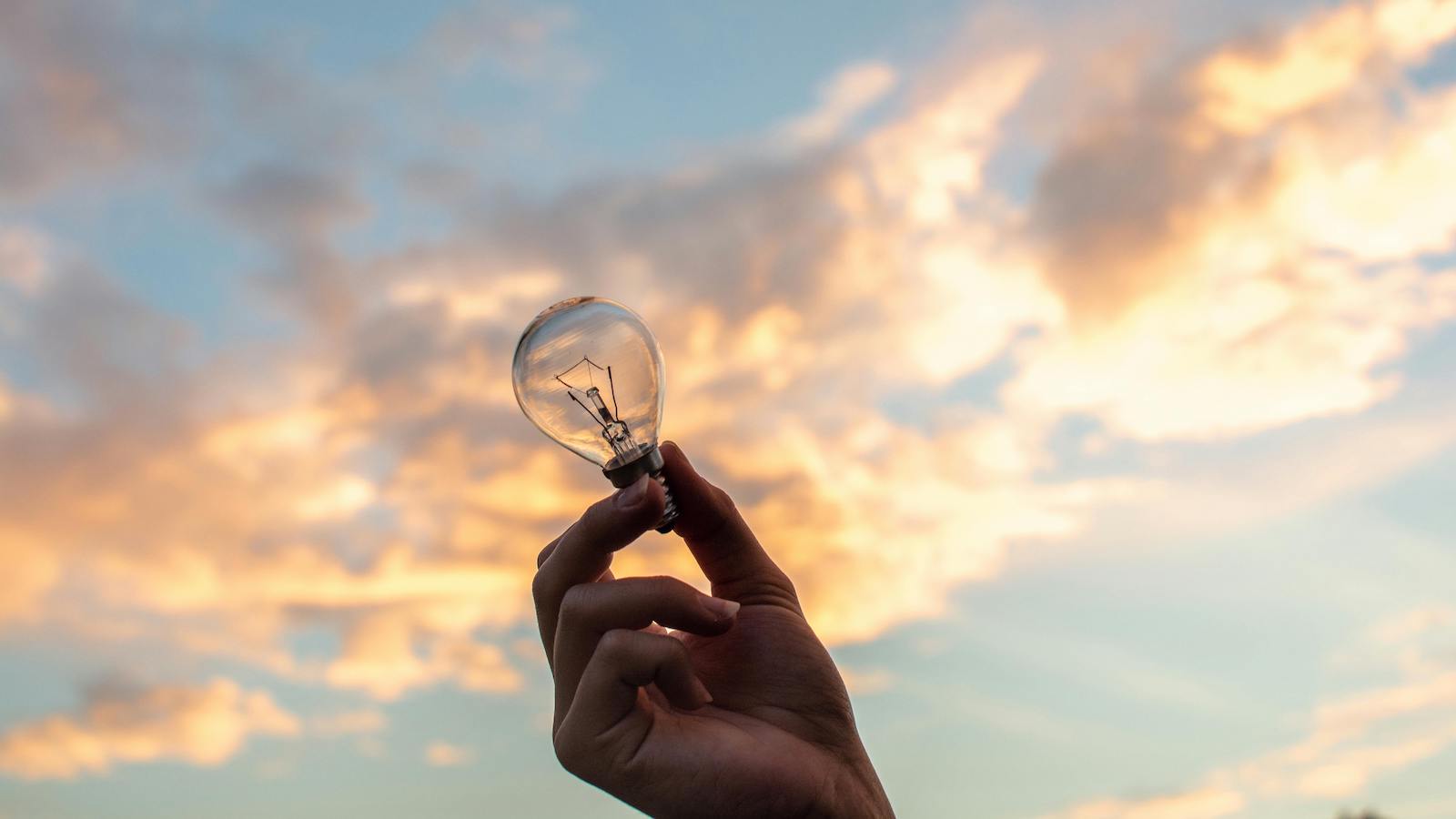 Person Holding Clear Light Bulb With Sky Background