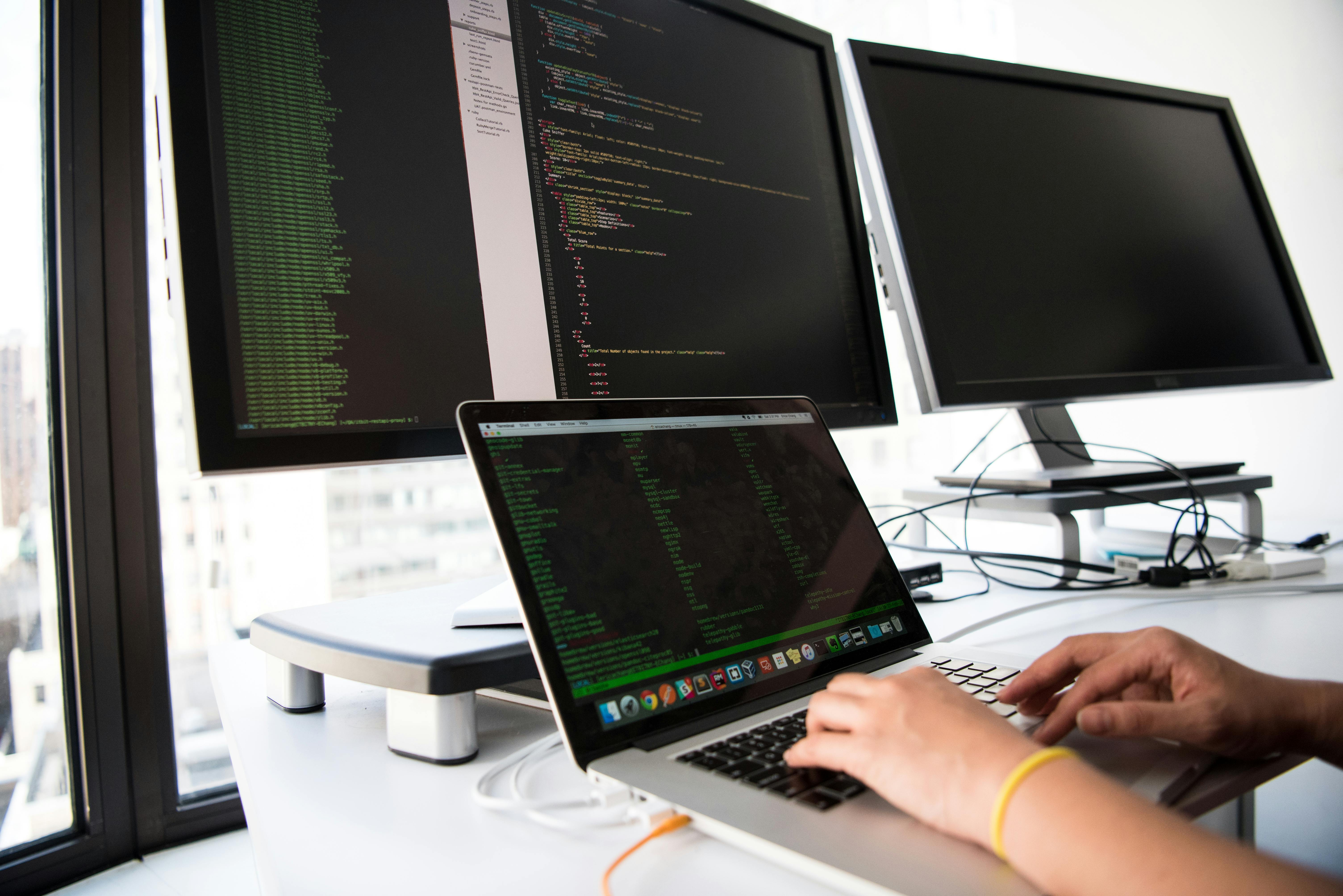 Shot of hands using a laptop in front of computer monitors