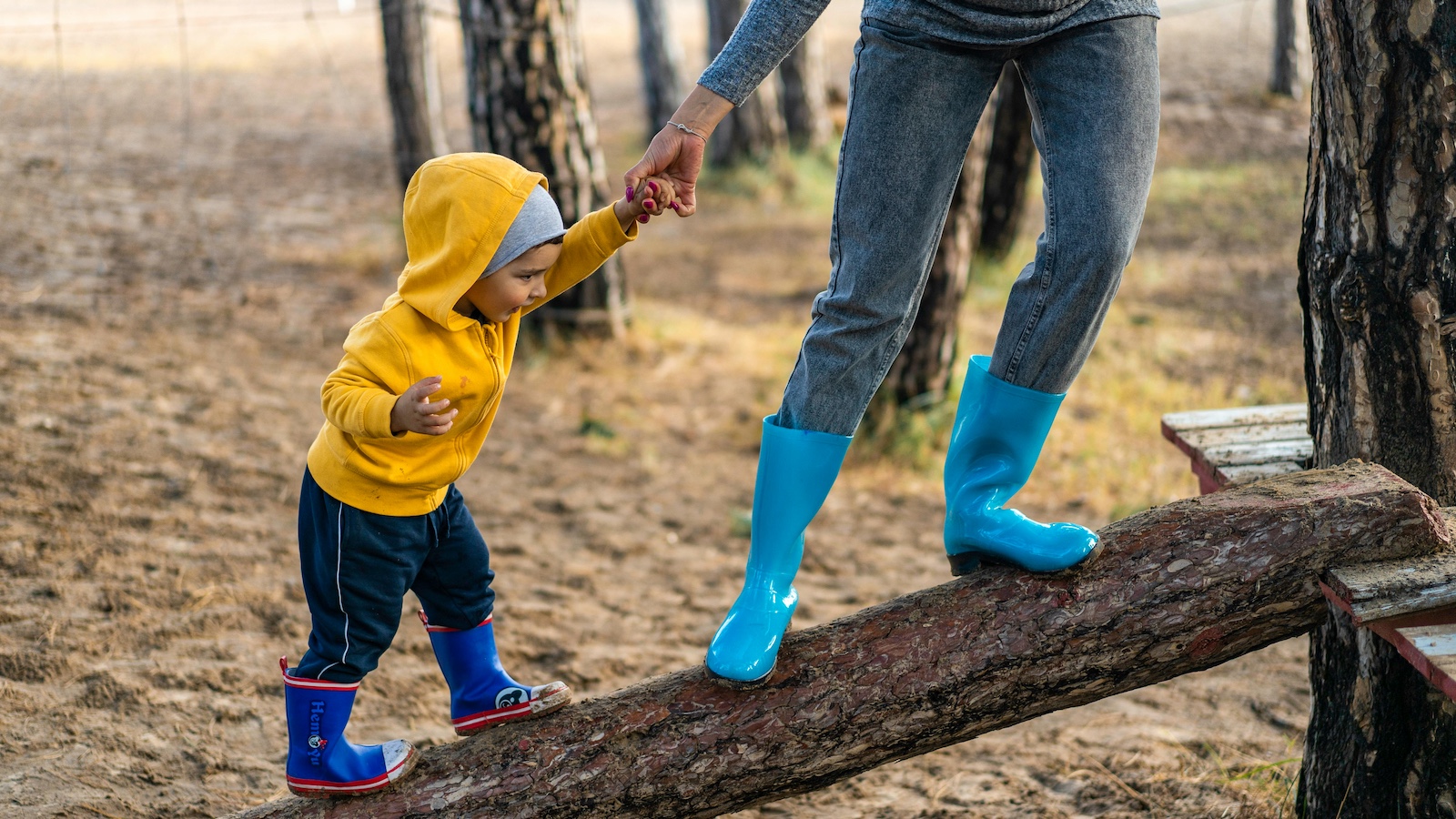 Toddler in yellow hoodie being led up a log