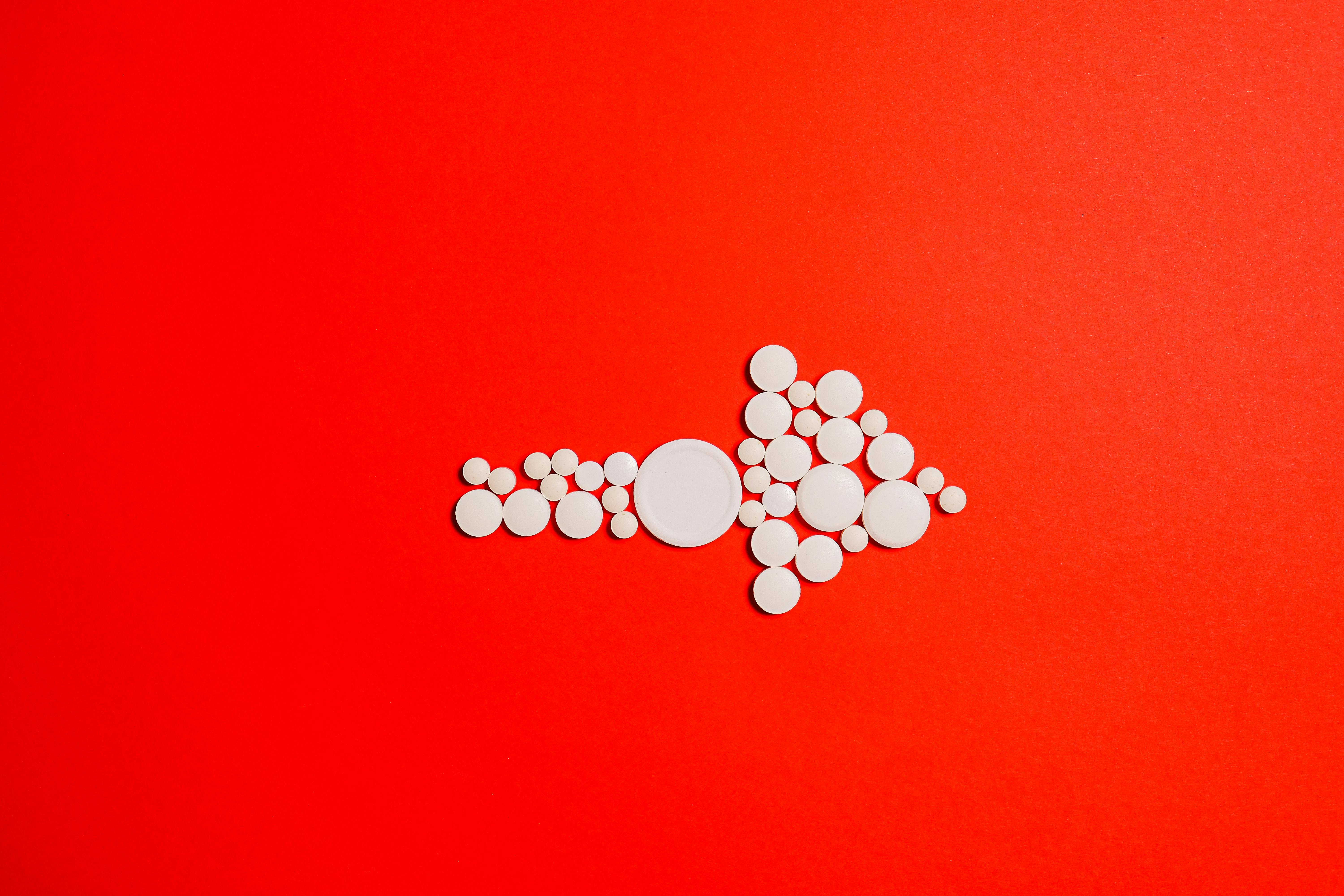 White Round Medication Pills In Shape of Arrow on Red Surface