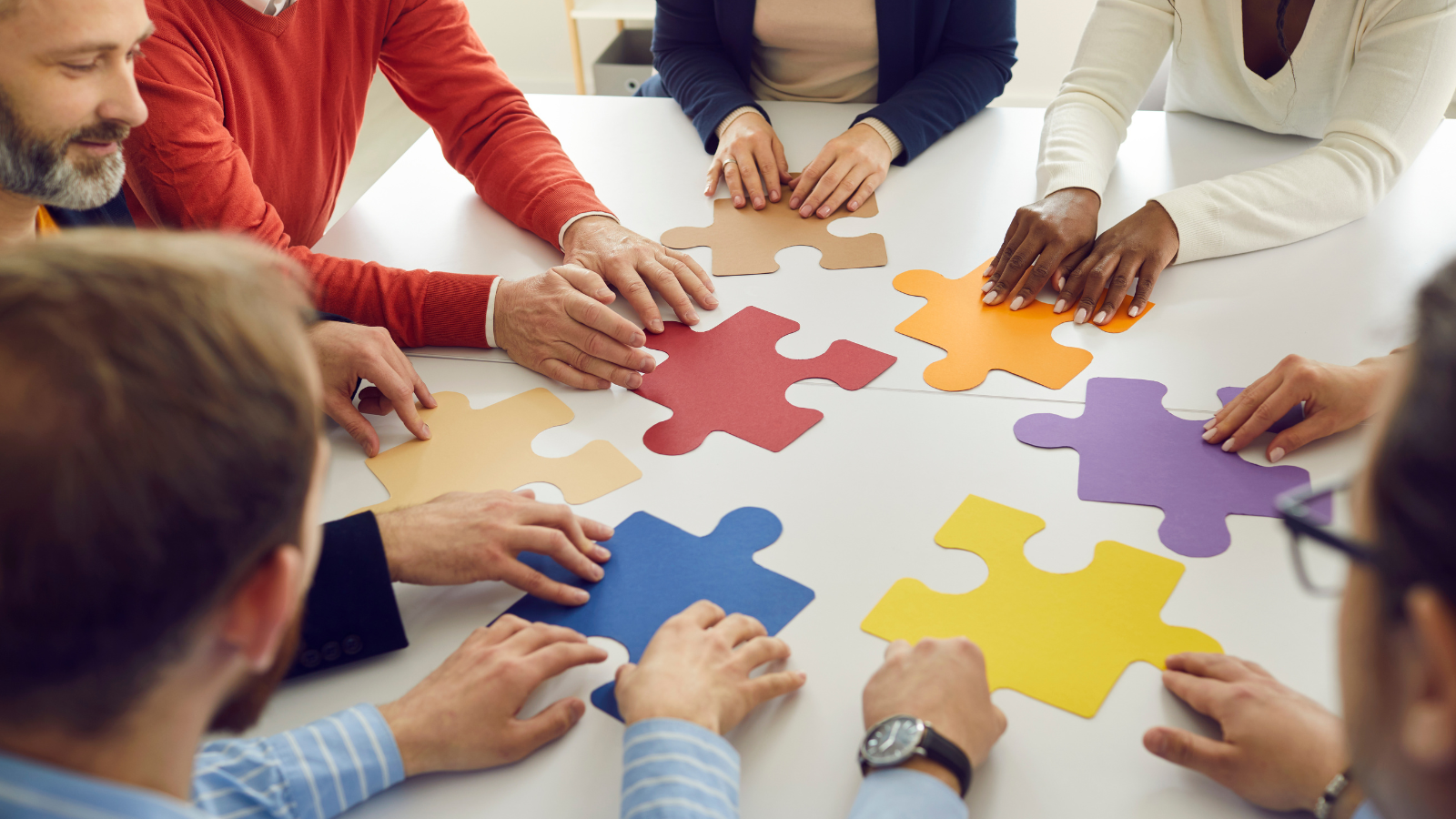 Large colorful puzzle pieces being put together by 6 different people