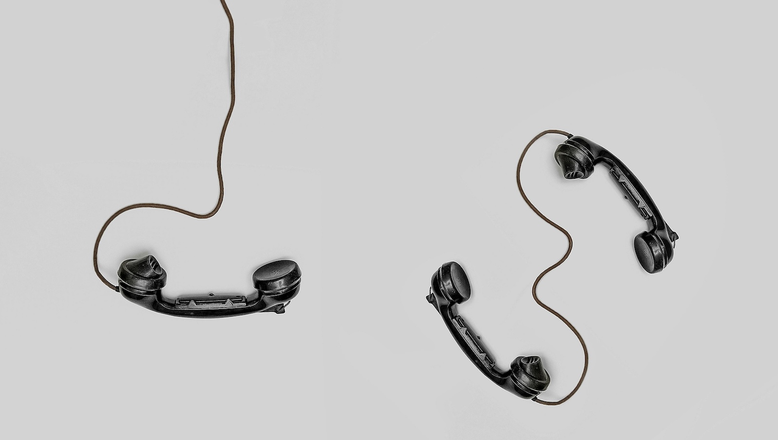 Three black old fashioned phones with cords against a grey solid background