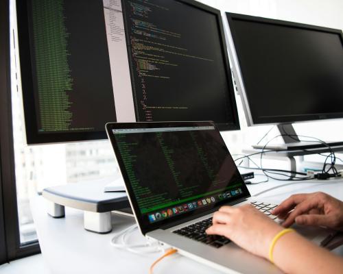 Shot of hands using a laptop in front of computer monitors