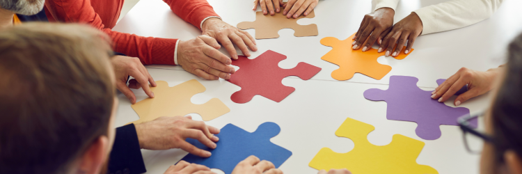 Large colorful puzzle pieces being put together by 6 different people