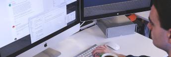 Man at a desk with a computer open and typing on a keyboard with a green mug of coffee in front of him