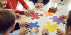 Large colorful puzzle pieces being put together by 6 different people